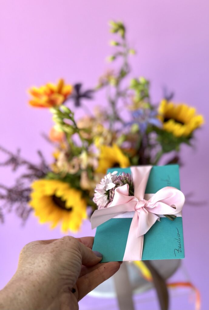 Teal greeting card with pink ribbon and flower arrangement out of focus in the background