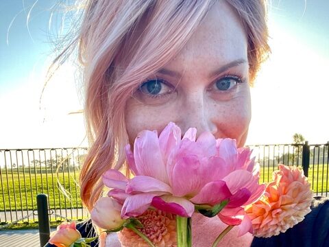 Woman holding pink peony in front of face